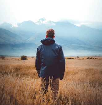 Man standing in grassy field with mountains in distance